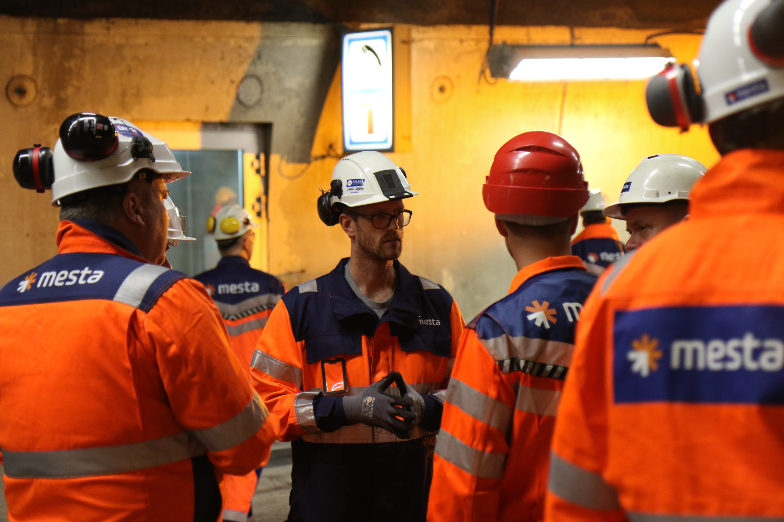 Fem Mesta-ansatte med hjelm og Mesta-klær på arbeid innendørs